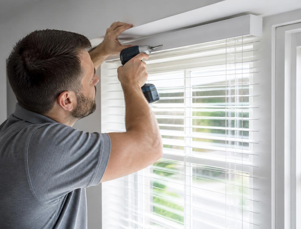 Handyman drilling new white blinds above a sunny window